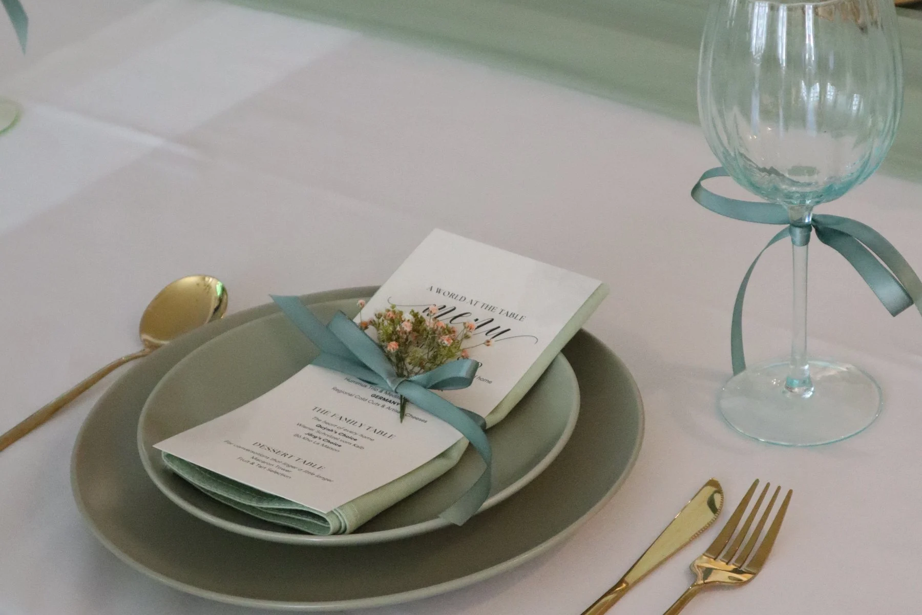 Place setting with menu card, gold cutlery and sage-green ribbon at a private event in Neuss